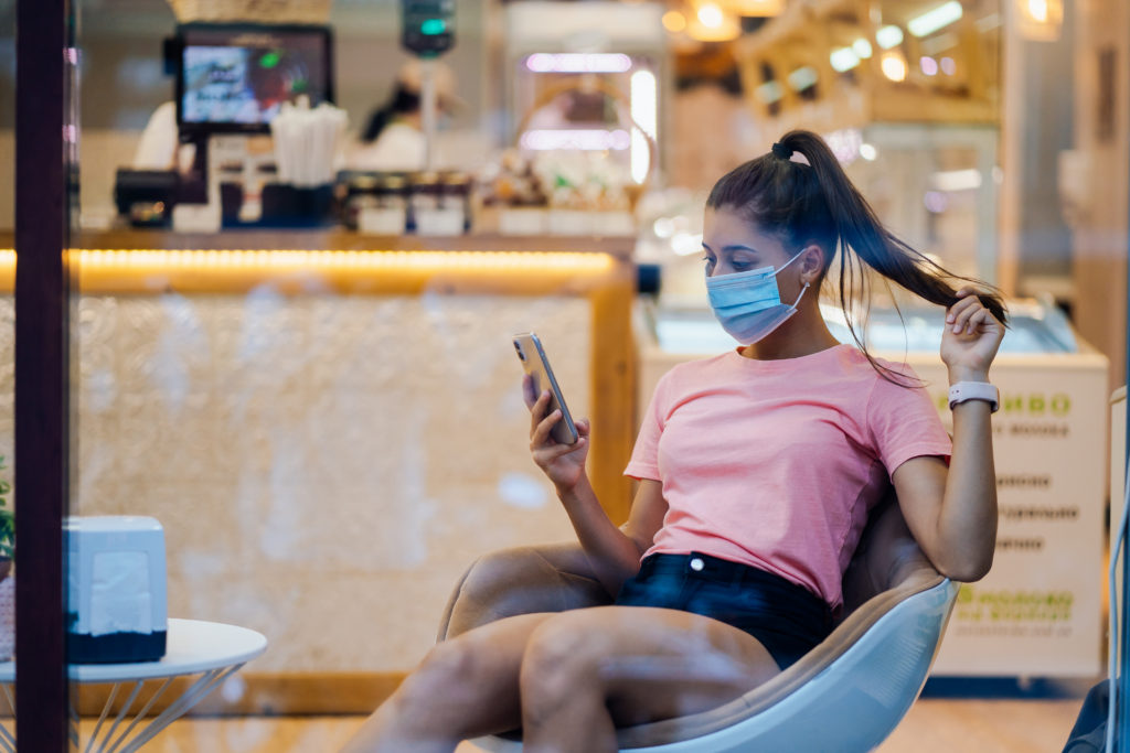 Woman with face medical mask using smartphone in cafe.